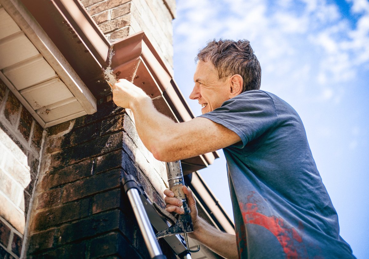 Worker sealing gutter on roof for property maintenance