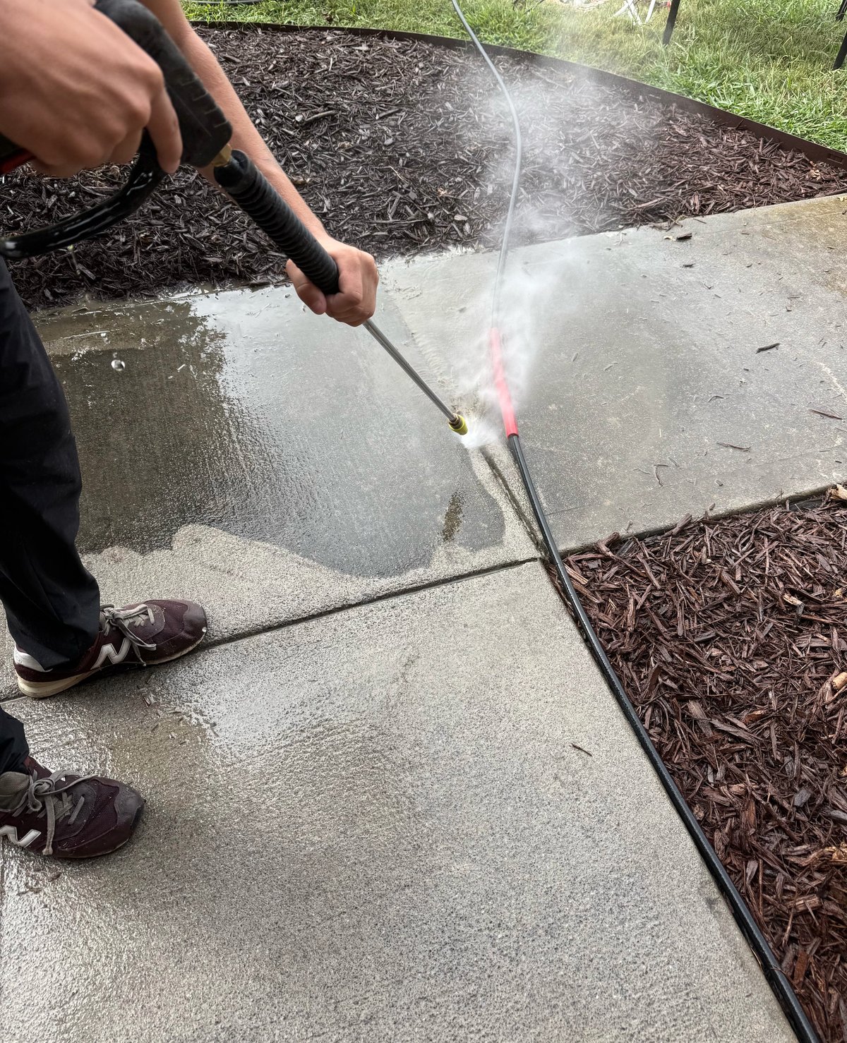 Brock Property Services crew member pressure washing a concrete sidewalk, revealing clean pavement beneath the grime